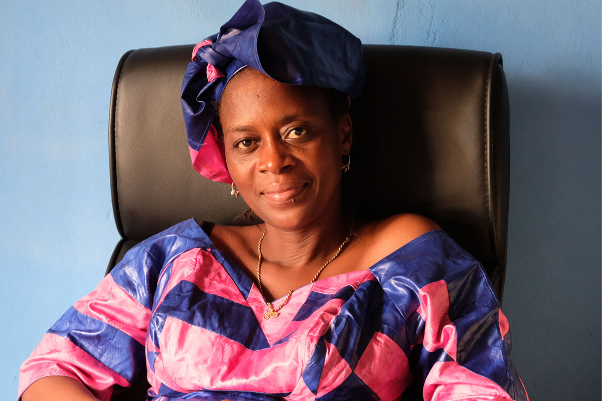 Portrait Rugiatu "Neneh" Turay © Terres des Femmes Portrait von Rugiatu "Neneh" Turay, einer Frau mit dunklem Teint in rosa-violetter Kleidung und passendem Turban, auf einem Stuhl sitzend