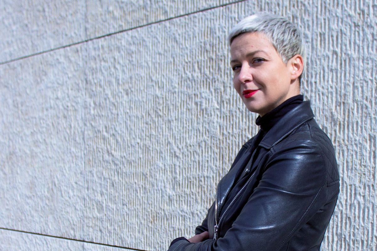 Maria Kalesnikava, Foto © Julia Schäfer Portrait von Maria Kalesnikava: Eine junge Frau mit graublondem Pixiecut, roten Lippen und in schwarzer Lederjacke blickt vor einer hellen Mauer stehend seitlich in die Kamera