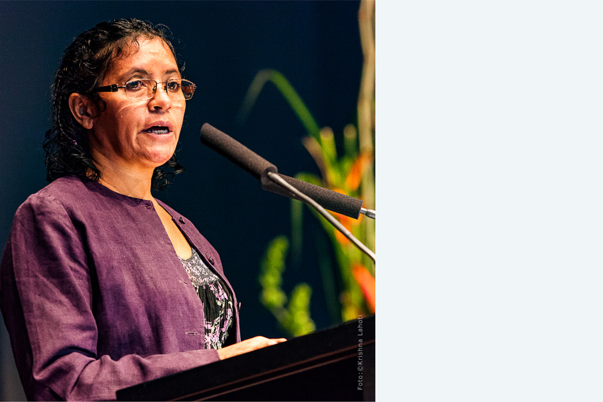 Laisa Santos Sampaio © Krishna Lahoti Frau mit dunklen Locken und Brille in violetter Jacke spricht am Rednerpult in ein Mikrofon