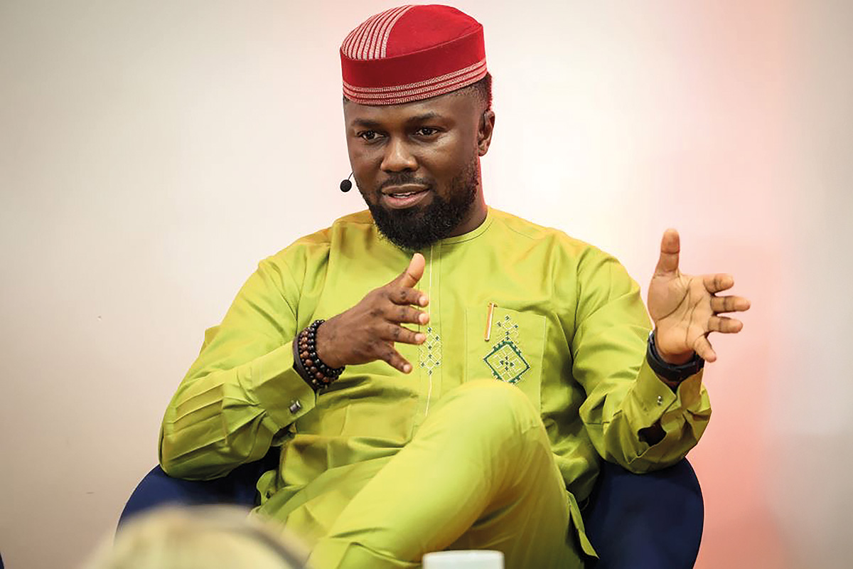 Philip Obaji Jr. ©Philip Obaji Jr. Portrait eines Mannes in hellgrüner Kleidung und mit roter Kopfbedeckung, mit einem Headset-Mikrofon und mit den Händen sachlich gestikulierend