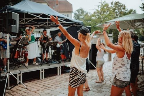 vor einer Bühne im Freien, auf der eine Band spielt, tanzen junge Frauen in Sommeroutfits