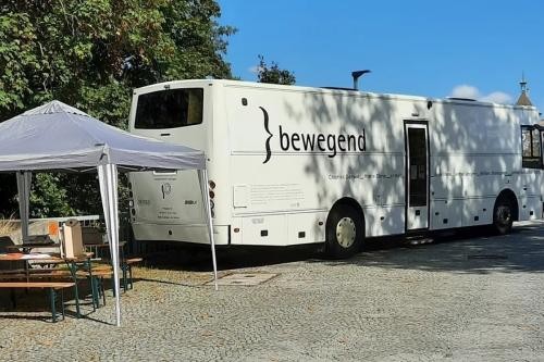 Pavillon mit Biertischgarnitur neben großem weißen Bus mit der Aufschrift "bewegend"