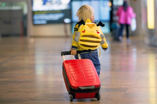 Kind mit Rollkoffer und Rucksack am Flughafen