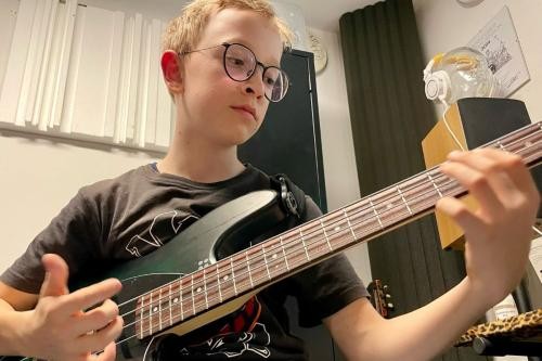 blonder Junge mit Brille spielt E-Bass