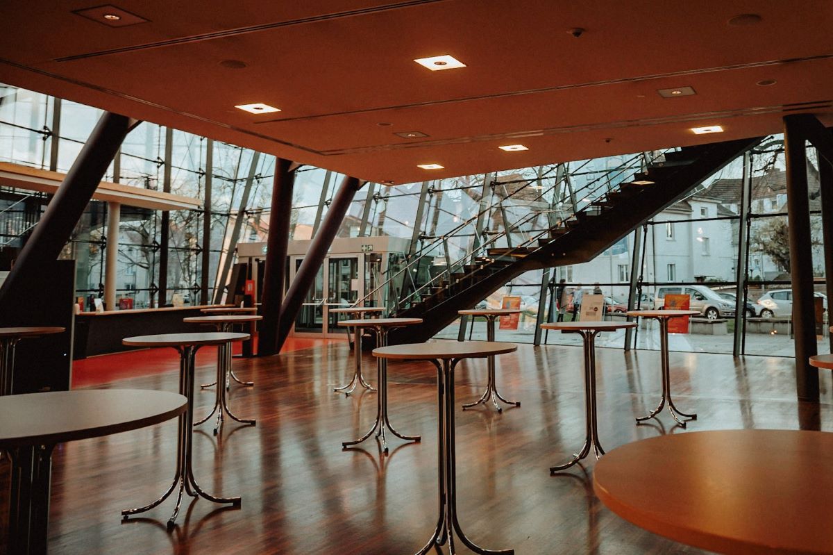 Foyer einer Halle mit Treppe, Glasfronten und vielen Stehtischen