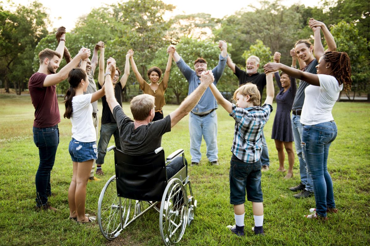 Inklusion Gruppe mit Rollstuhlfahrer steht im Kreis und hält sich an den Händen.