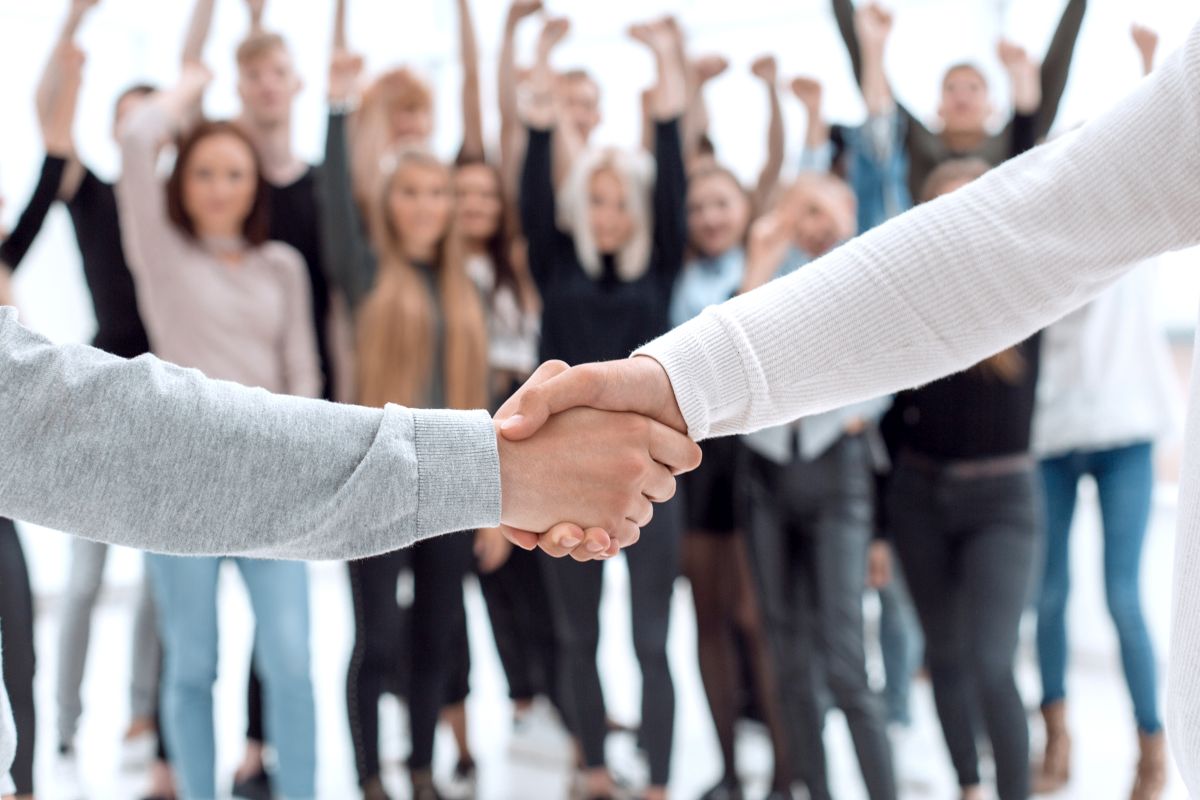 Karriere Zwei Personen geben sich die Hand. Im Hintergrund jubelt eine Gruppe menschen.