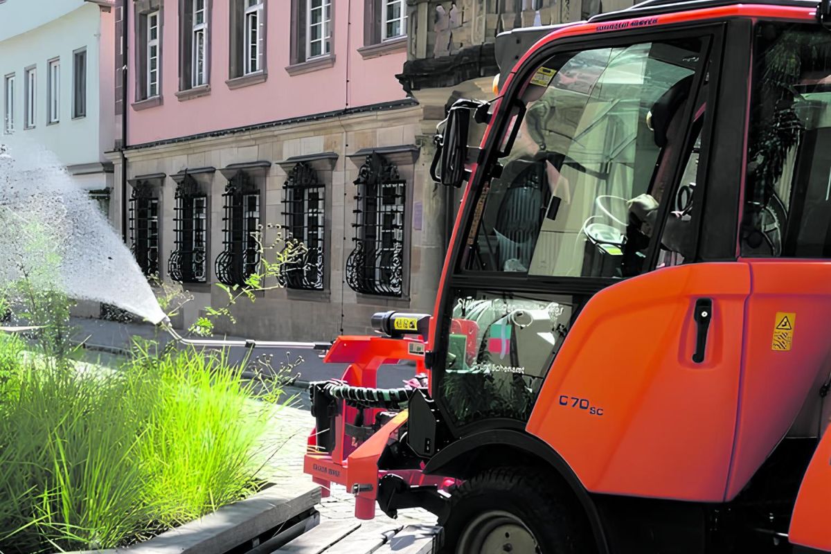 Traktor mit Gießarm wässert ein Blumenbeet