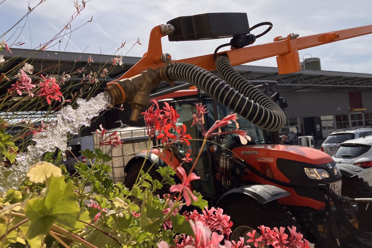 Traktor mit Gießarm wässert ein Blumenbeet