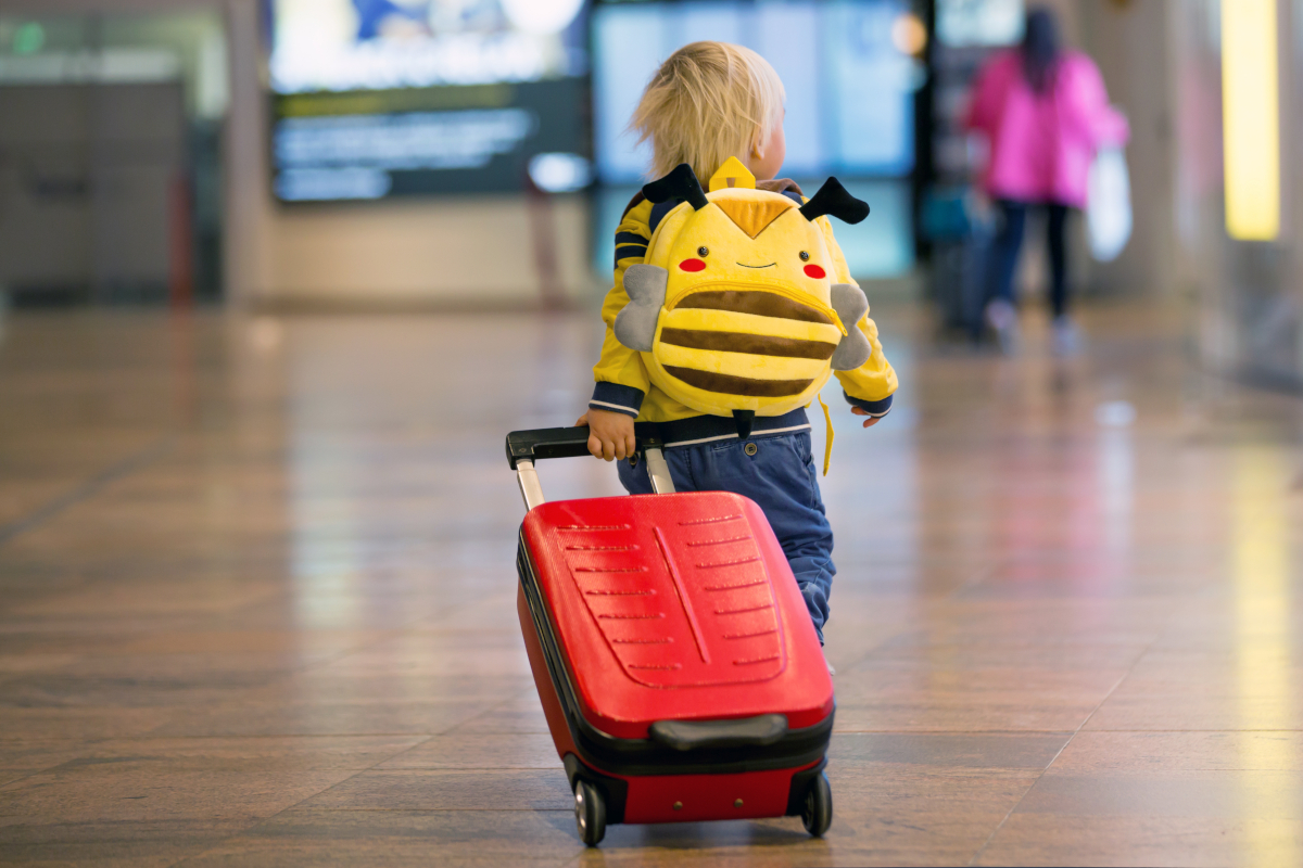 Kind mit Rollkoffer und Rucksack am Flughafen