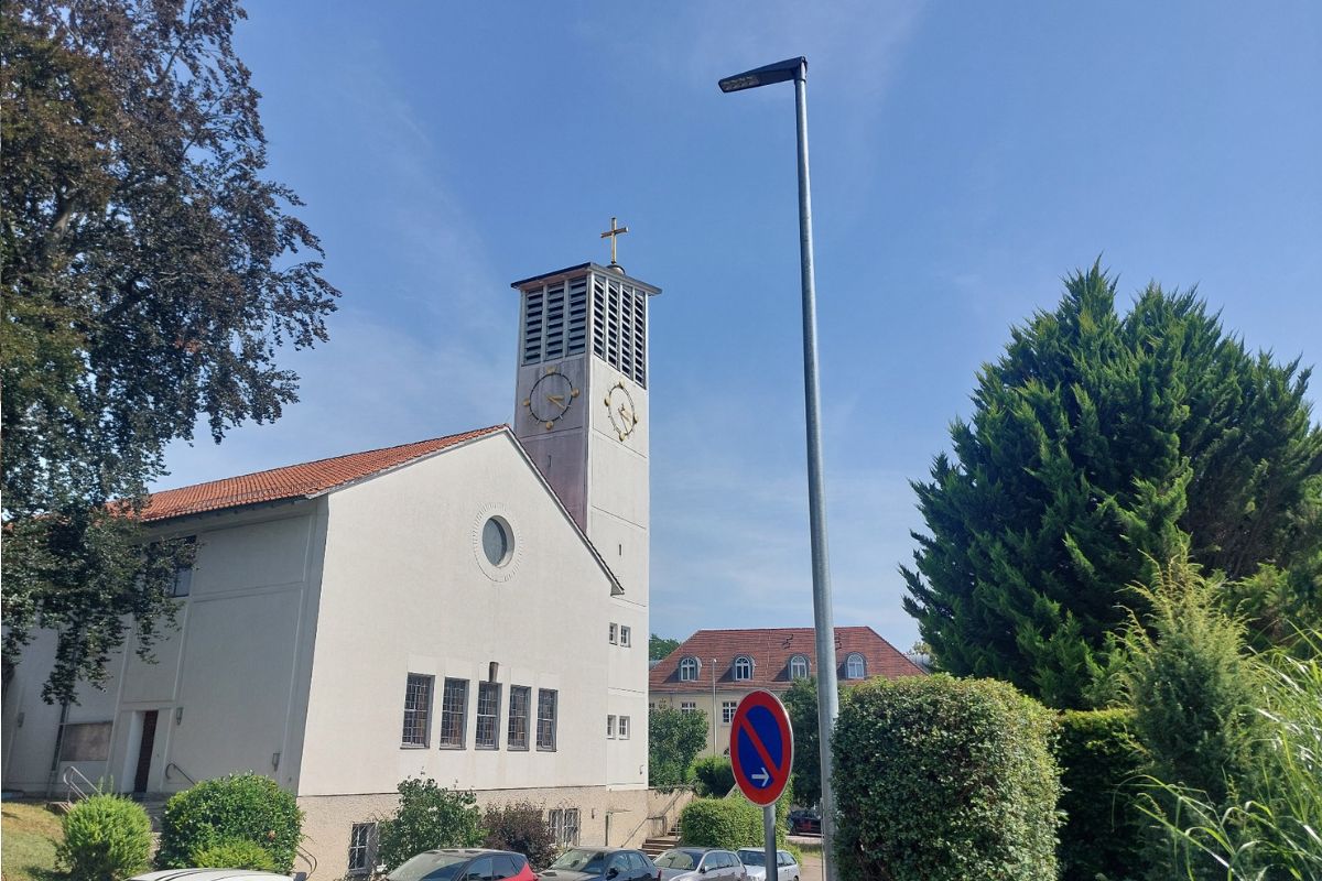 Zu sehen ist eine moderne Straßenlaterne mit LED-Leuchte. Im Hintergrund steht die Kirche St. Bernhardt in Esslingen-Hohenkreuz