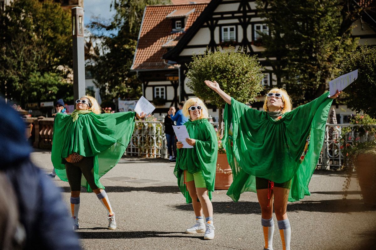 drei Frauen in grün mit gelben Perücken performen auf der Straße