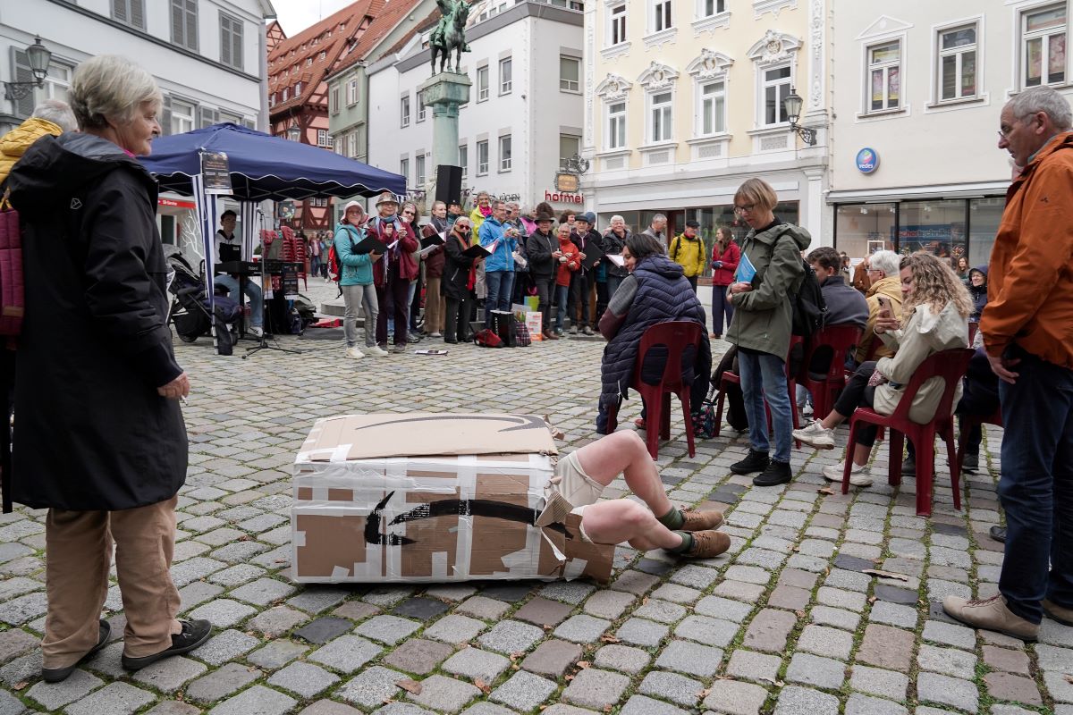 Kunstperformance auf Kopfsteinpflaster: Person liegt in einem Karton im öffentlichen Raum