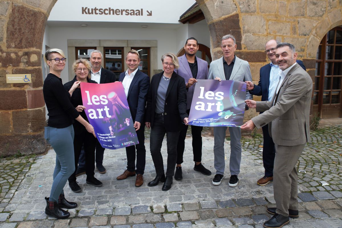 Neun Personen gruppieren sich um zwei lesart-Plakate vor dem Eingang zum Kutschersaal der Stadtbücherei