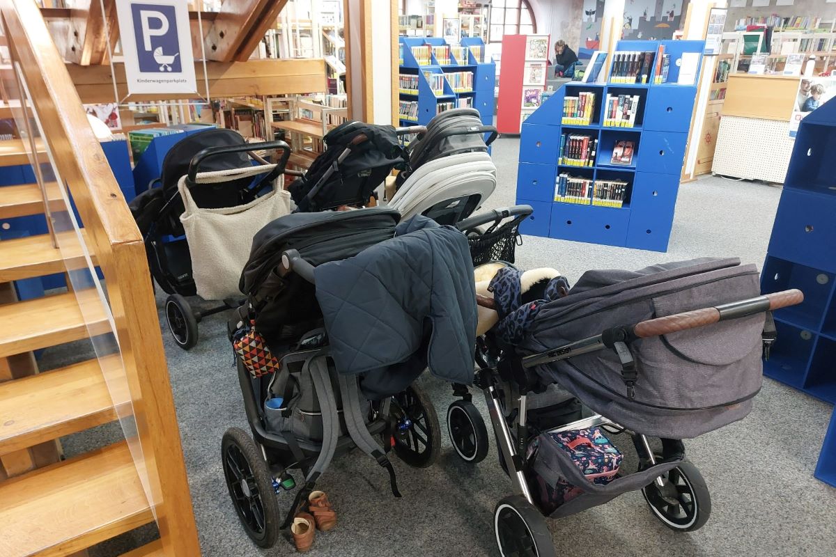 Kinderwägen stehen unter einer Treppe, im Hintergrund Bücherregale