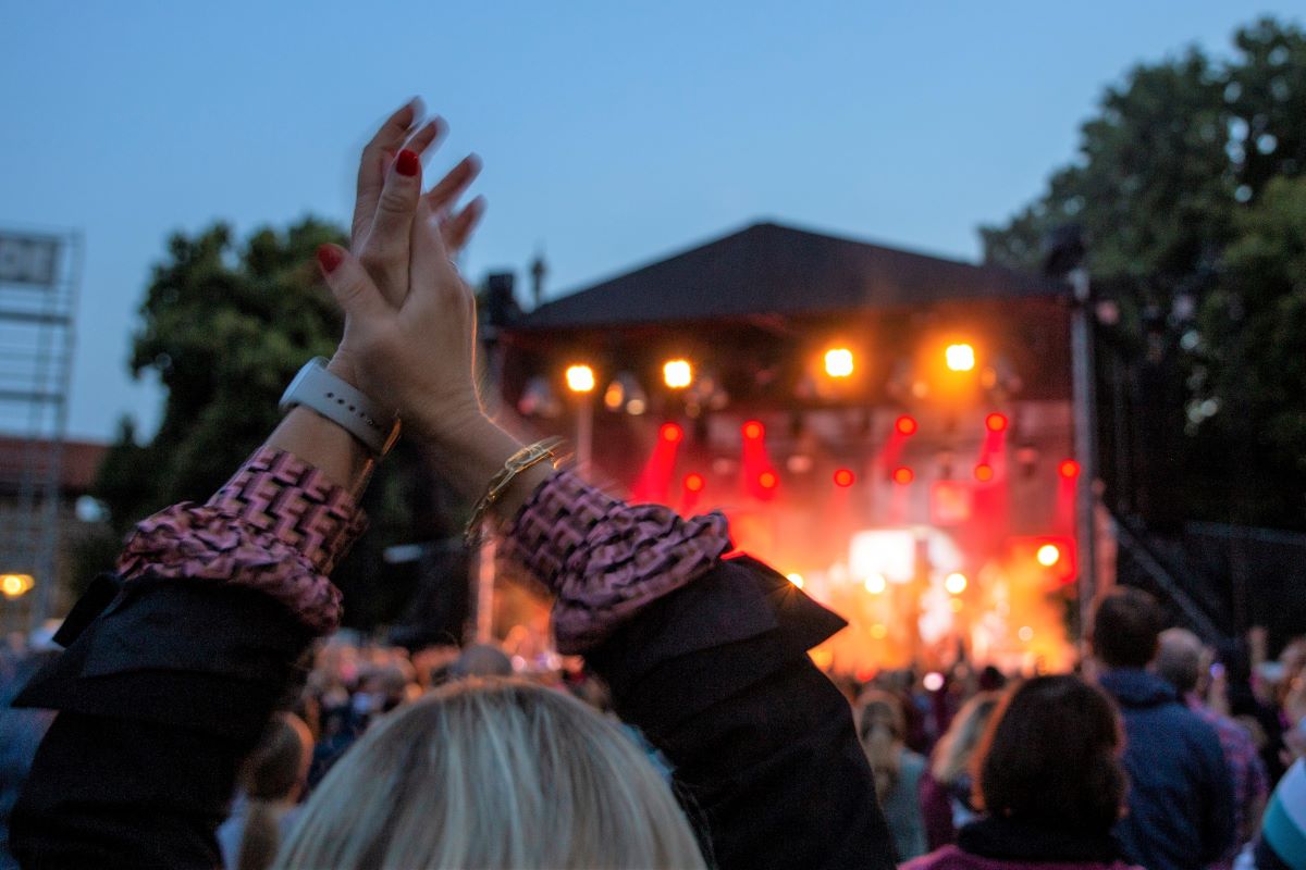 Konzertbühne, Open air, im Vordergrund klatscht eine Frau über ihrem Kopf in die Hände