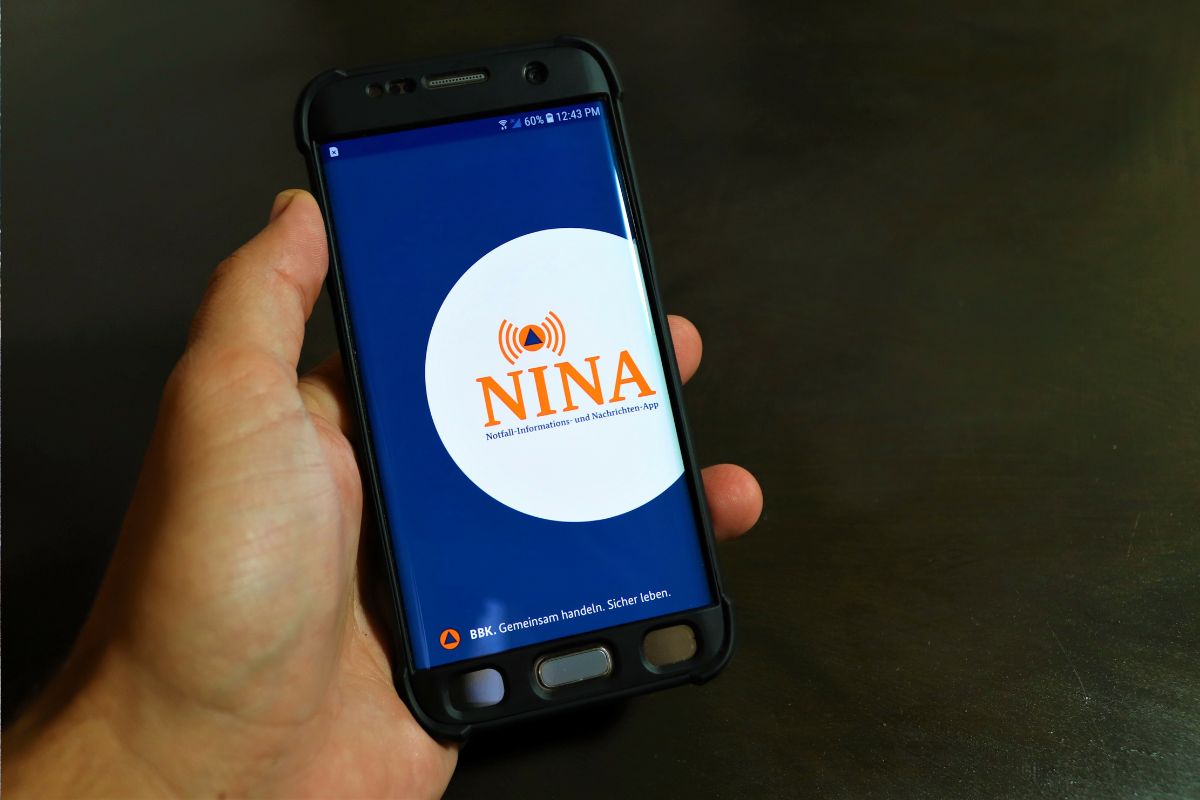 Eine Hand hält ein Smartphone, auf diesem ist die NINA-Warn-App zu sehen