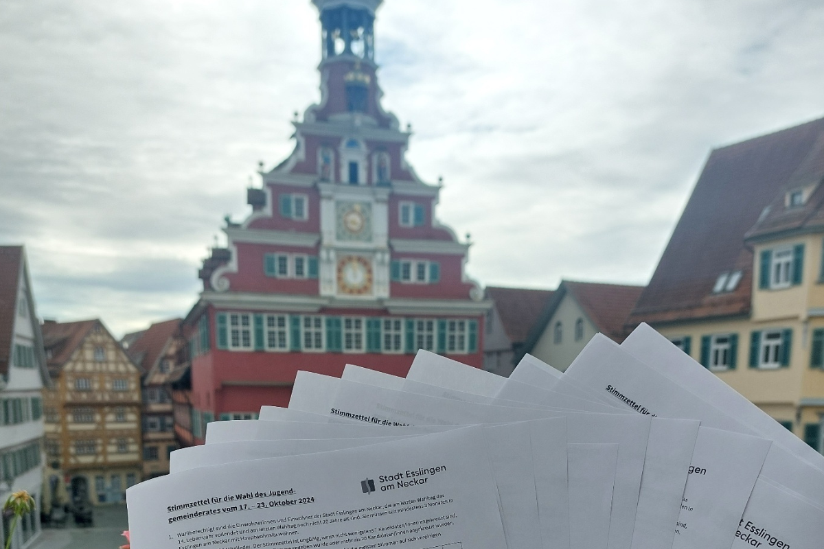 Zu sehen ist das Alte Rathaus in Esslingen, davor werden die Stimmzettel der Jugendgemeinderatswahl gehalten.