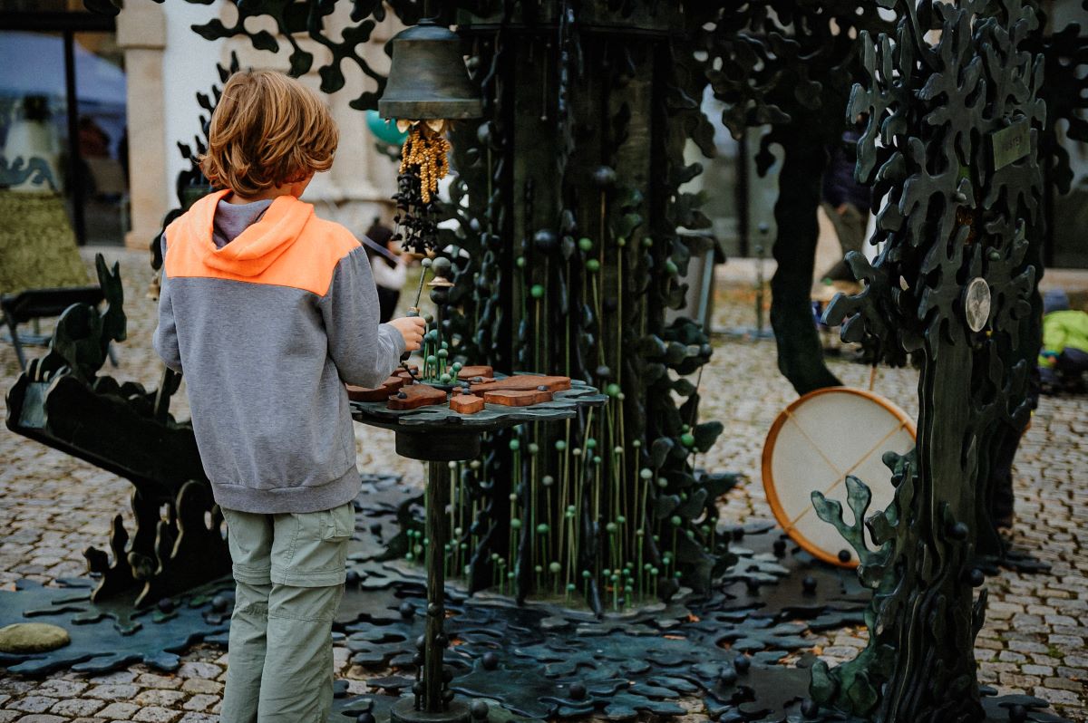 Das Waldorchester © Sabine Watzko Kind spielt mit einer dunkelgrünen Installation mit Glocke