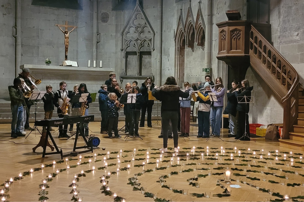 Ein Ensemble aus Jugendlichen und Kindern mit verschiedenen Blasinstrumenten musiziert vor einem Labyrinth aus Kerzen.