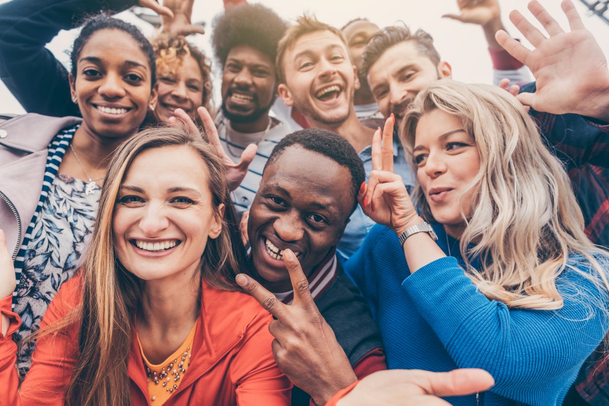 Fröhliche junge Menschen unterschiedlicher Herkunft machen das Peace-Zeichen.