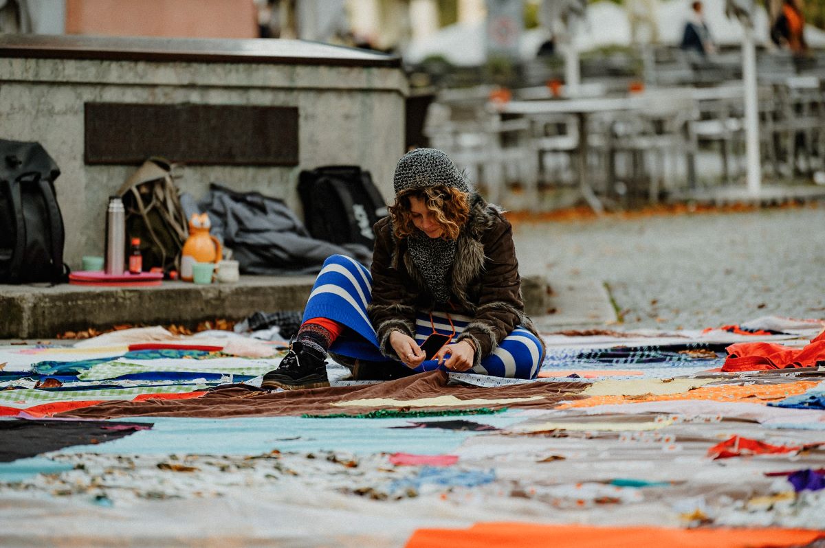 Eine Unterhaltung im Freien © Sabine Watzko Frau sitzt im Freien auf dem Boden und näht an einer riesigen Picknickdecke