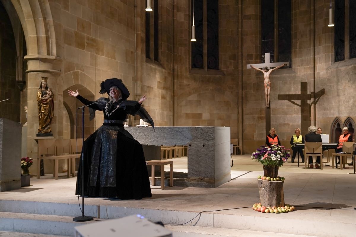 Frau performt in schwarzem Kleid mit Hut im Altarraum einer Kirche