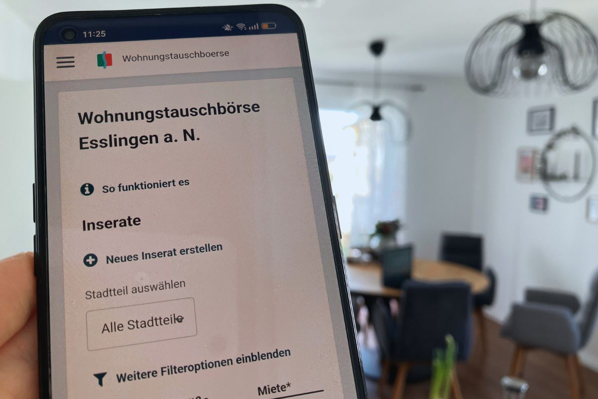 Auf einem Smartphone ist das Online-Portal der Wohnungstauschbörse zu sehen, unscharf im Hintergrund ein Esszimmer