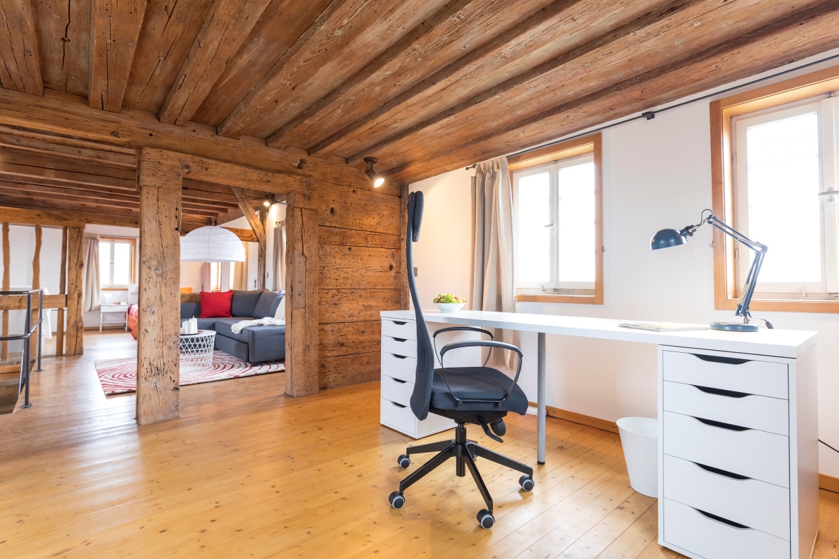 Arbeitsplatz mit Schreibtisch, Lampe und Stuhl in einem hellen, holzgetäfelten Raum