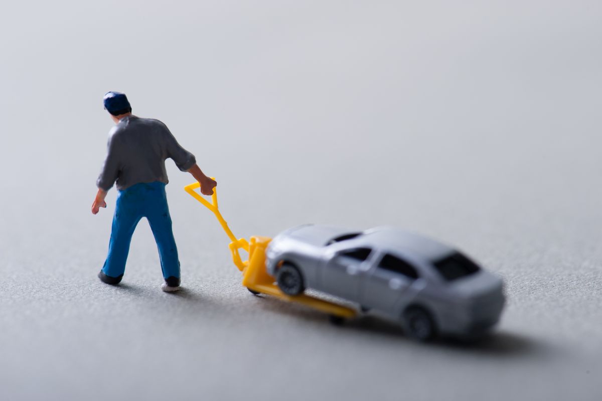 Abschleppen Spielfigur Mann zieht kleines Auto mit Hubwagen